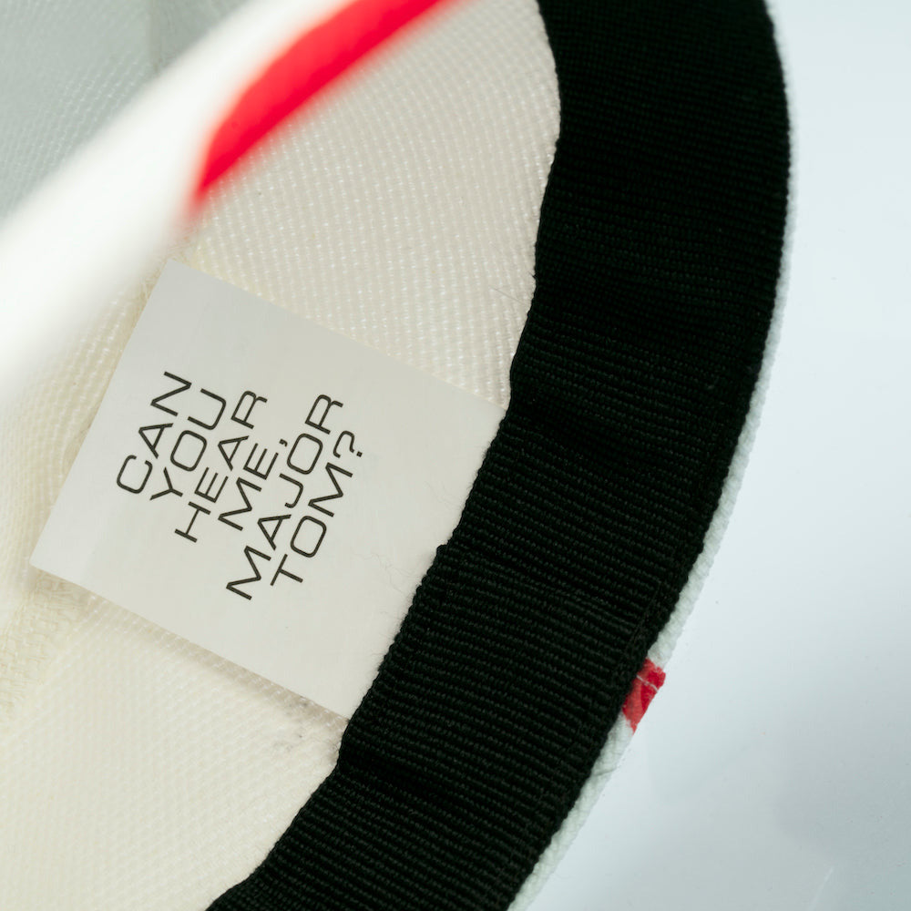 Close-up of a buckethat with a label reading 'Can You Hear Me Major Tom?' 