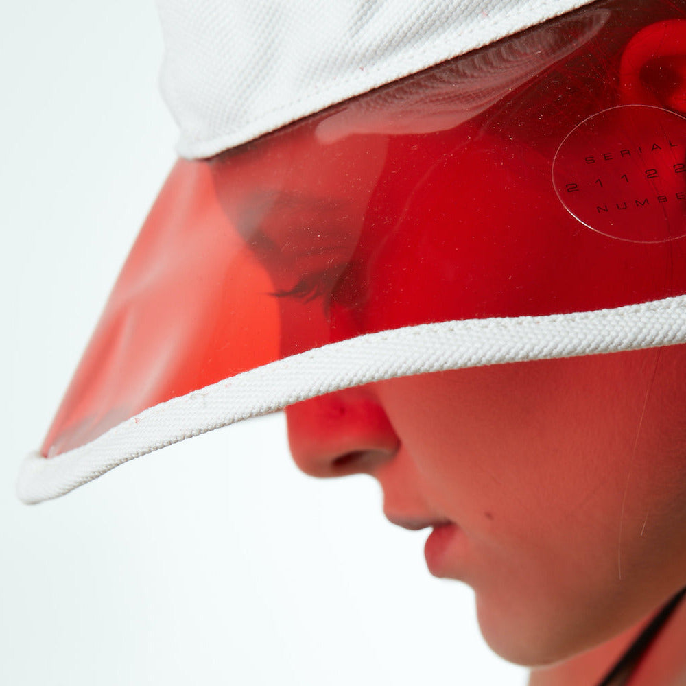 Close-up of a person wearing a red visor and white buckethat on a white background