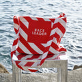 Red and white striped shoulder-bag with 'RACE LEADER' text on a chair by the water.