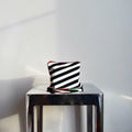 Black and white striped pouch on a metallic stool against a plain wall