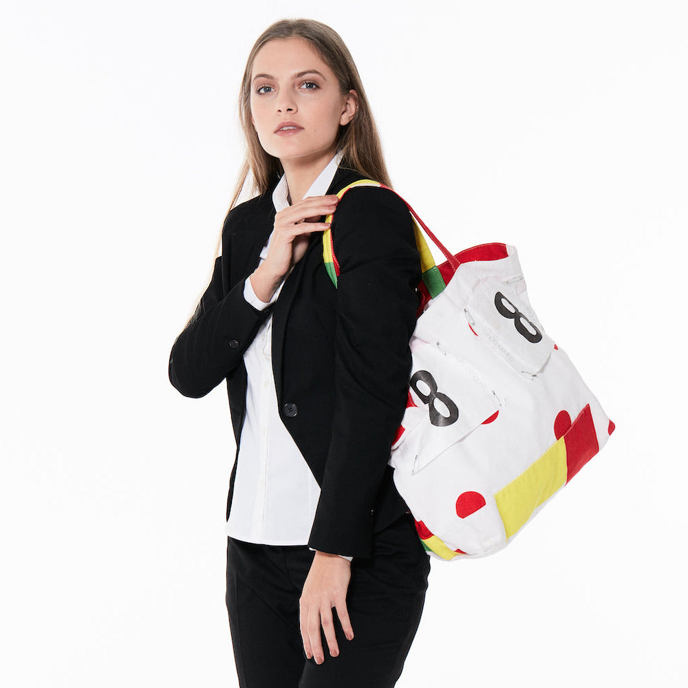 Woman carrying a white tote bag with number 8 with red polkadots and yellow accents, featuring Superleggero branding.